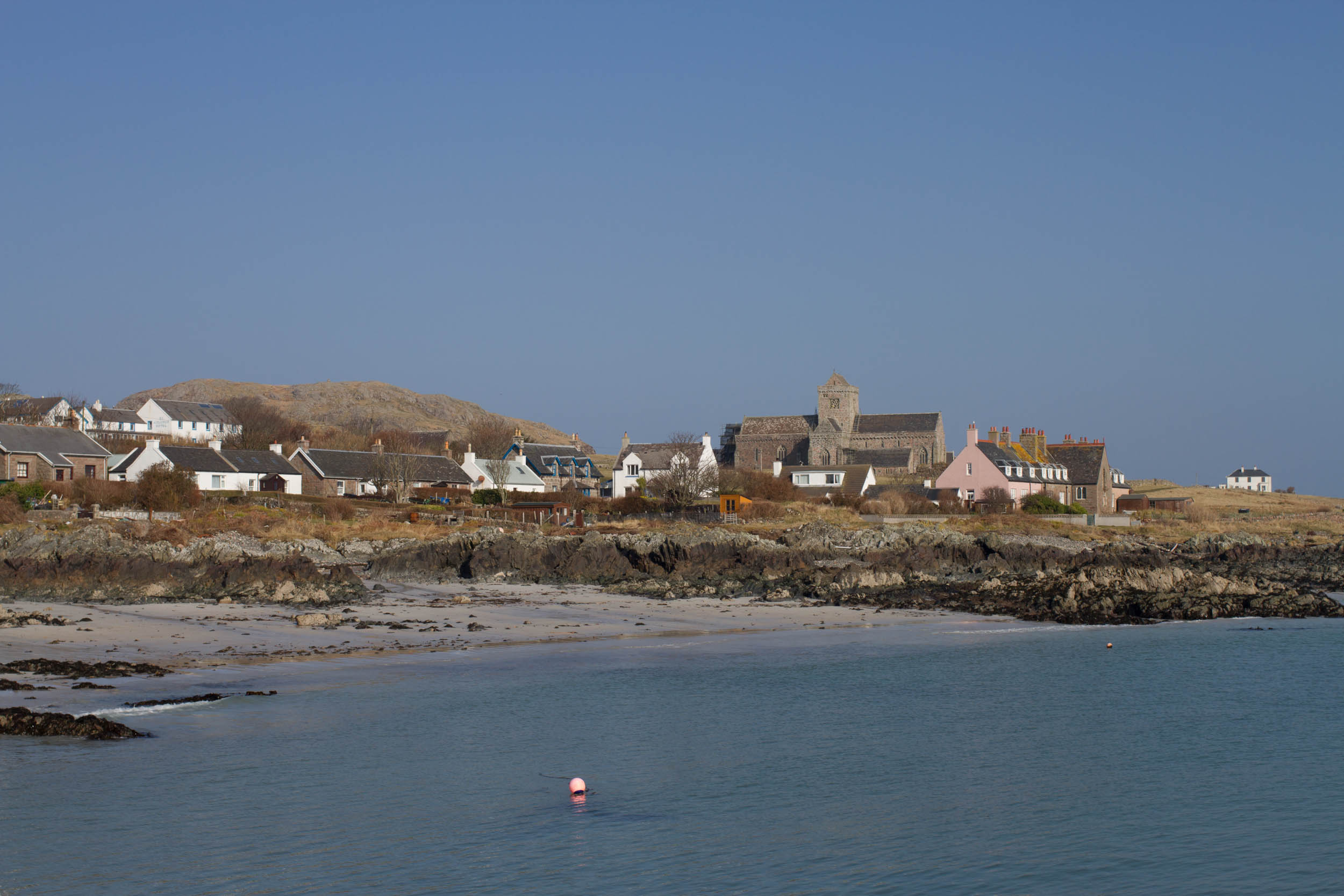 Photo of the coastline of the Isle of Iona. Houses and the Abbey overlooking the sea