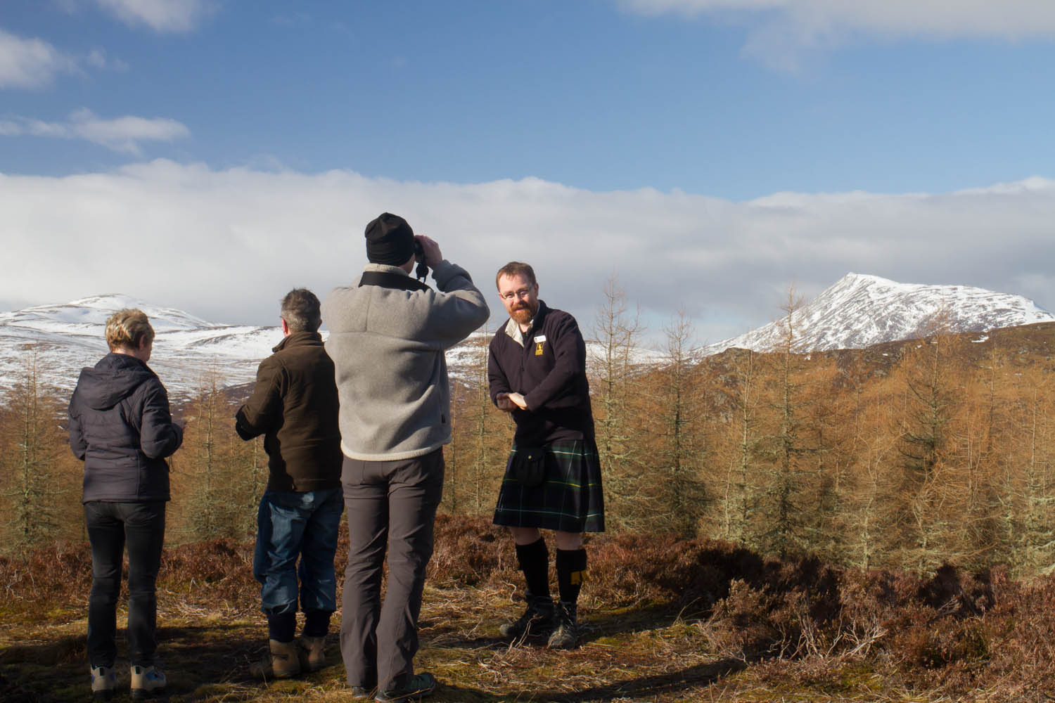 Highland Safaris, Perthshire. Tour guide in a kilt with a group of people on the hills. Man looking through binoculars