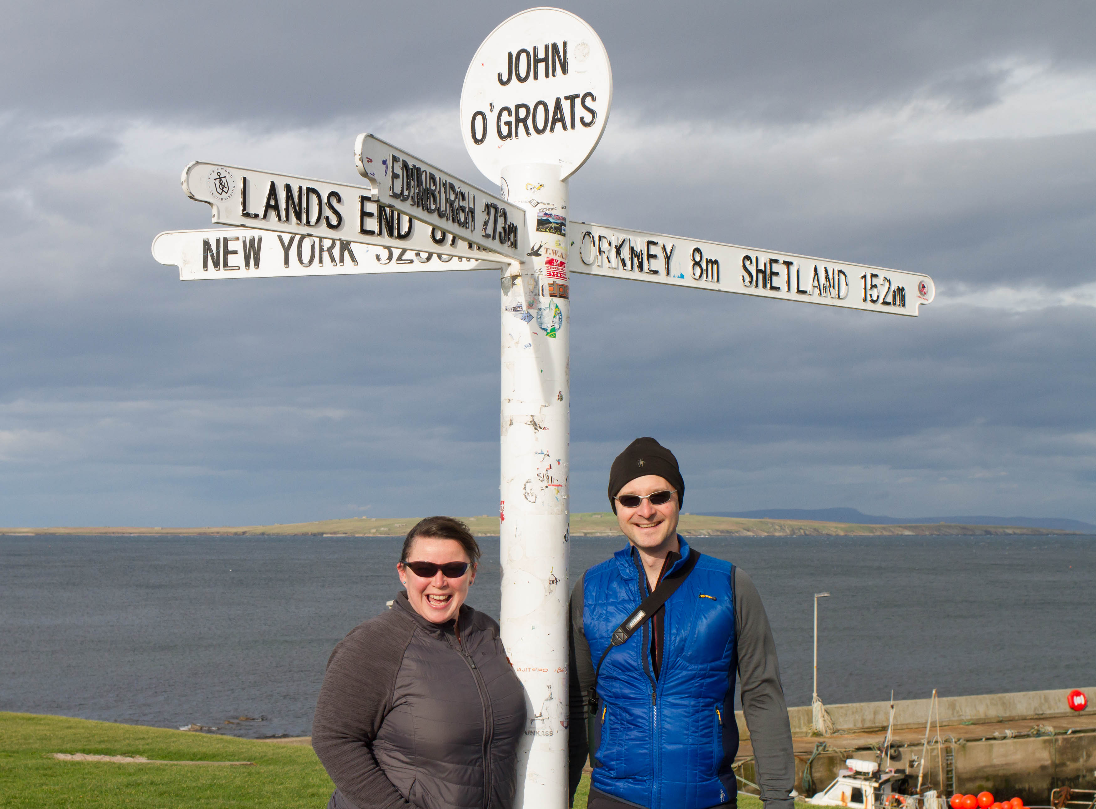 Scottish Travel Blogger. Man and woman stood beneath the John O'Groats mileage sign post. 