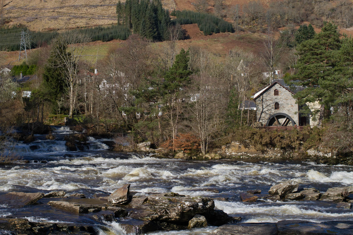 Falls of Dochart, Scotland. River running over large rocks. Watermill on the river bank surrounded by trees