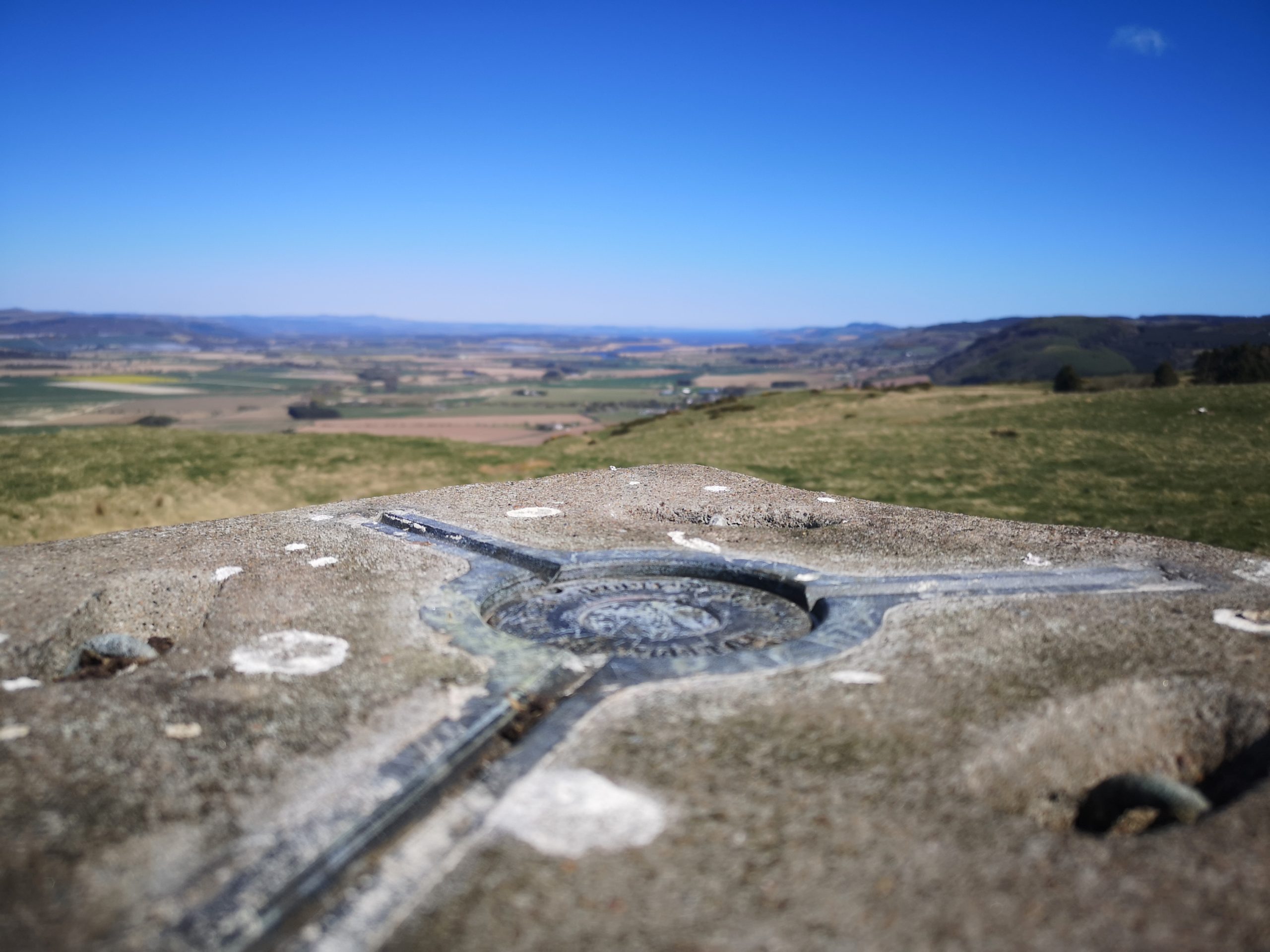 Photo of the top of a trig point. Countryside in the bckground