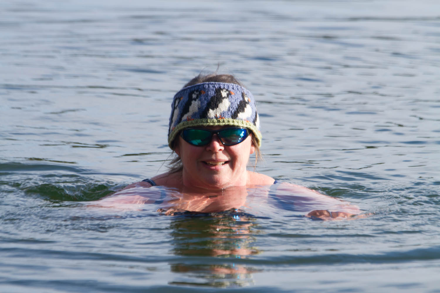 Photo of a woman in the water. The sun is shining and she is wearing sun glasses and a headband with puffins on