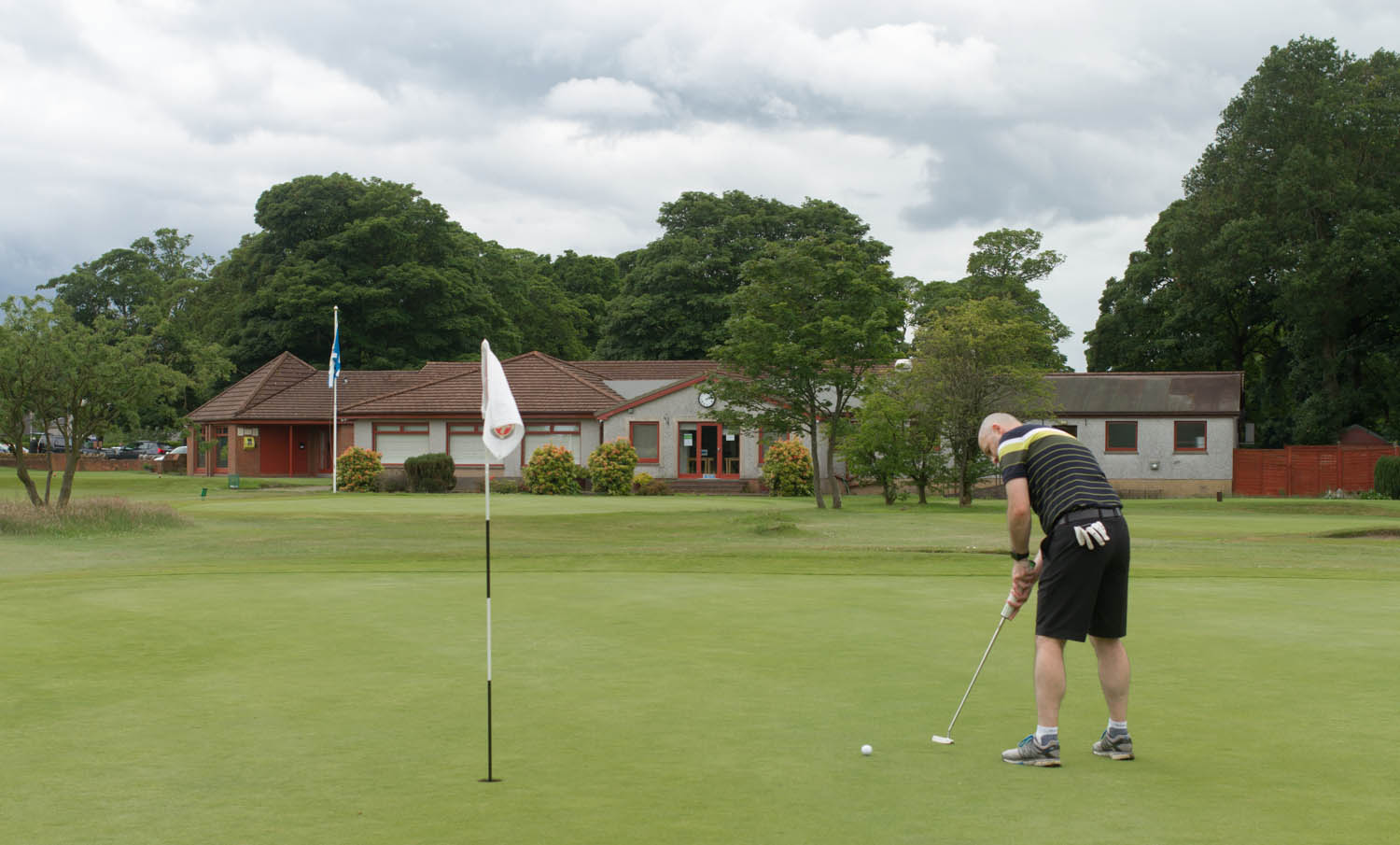 Photo of a man playing golf. He is putting on the 18th green