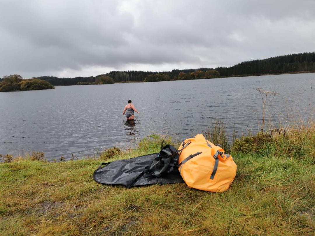 Image of a woman getting into to a loch for a cold water swim. Wild Swimming retreat at Creeside Escape