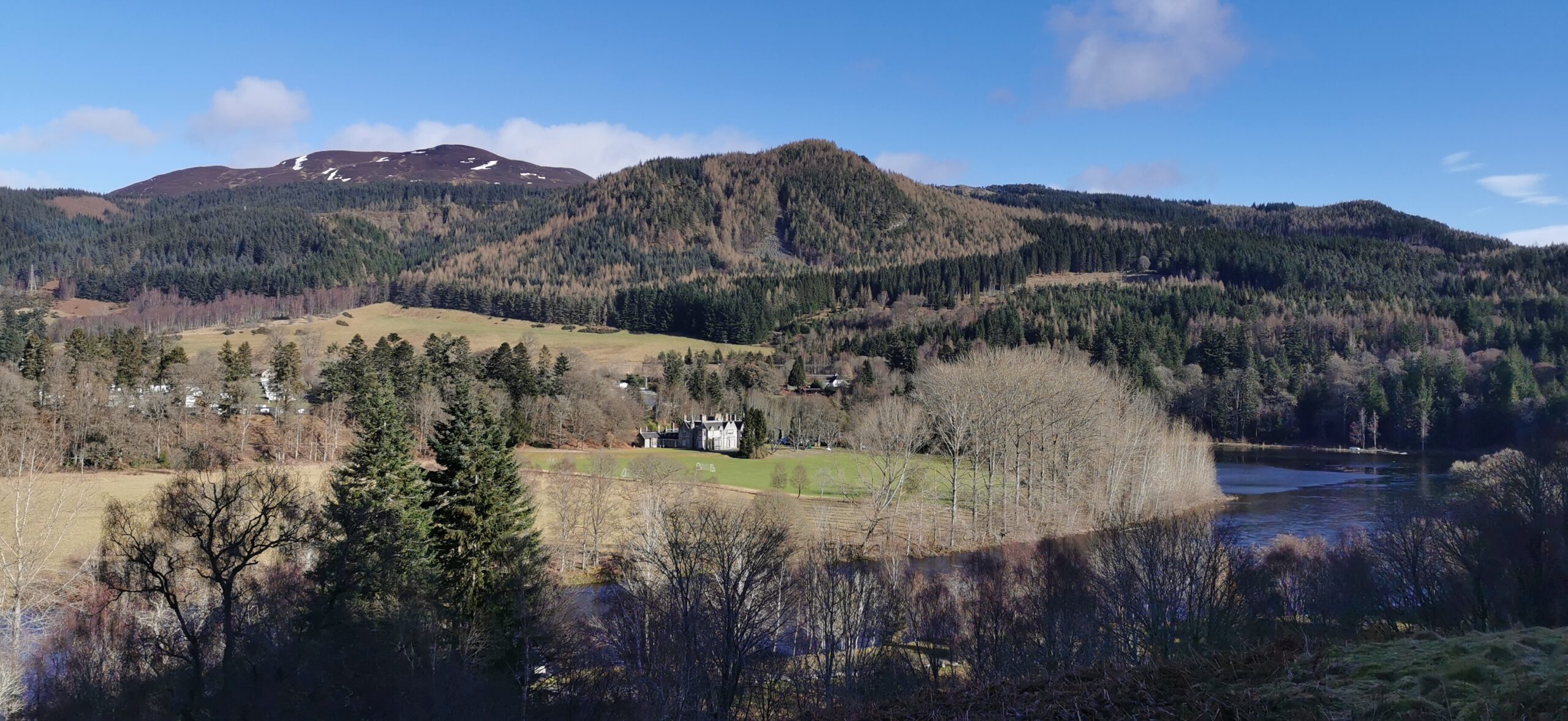 Image of: hills covered in trees. There is a small white house in the distance. 